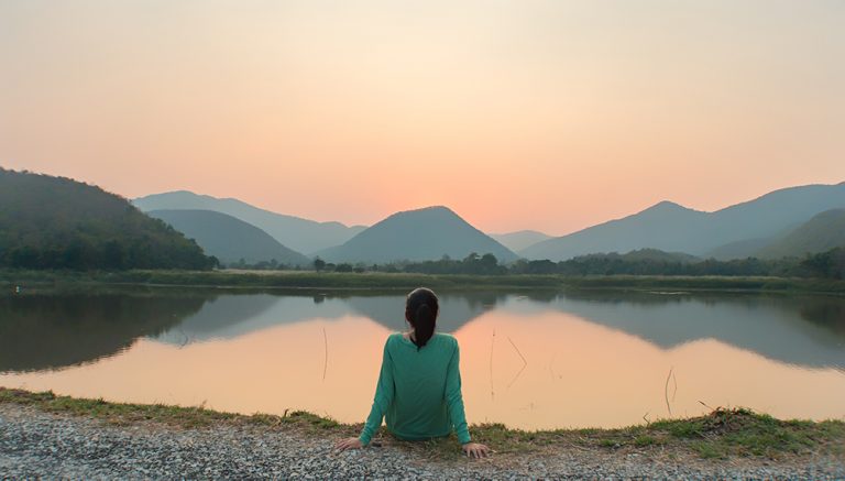 Frau entspannt an einem ruhigen See bei Sonnenuntergang