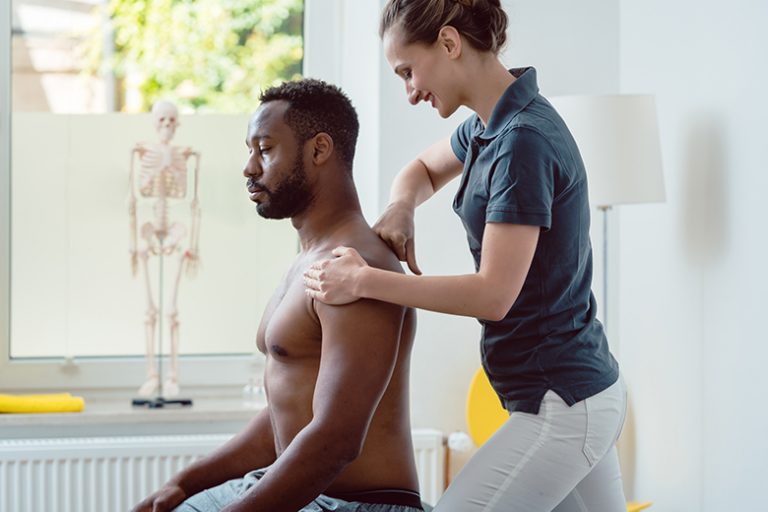 Physiotherapeutin behandelt Mann am Schulterblatt