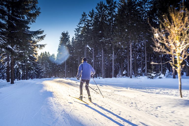 Mann skatet auf Langlaufskiern durch den verschneiten Wald