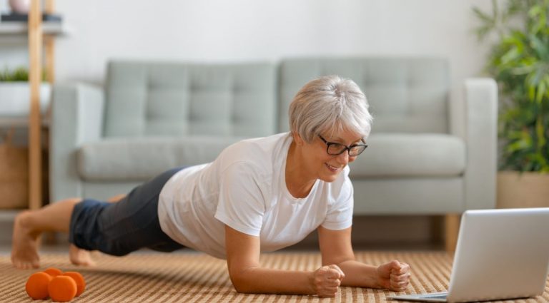 Ältere Frau macht eine Plank Zuhause vor dem Laptop