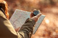 Active young woman holding a compass and reading a map while taking a hiking break, having fun and relaxing while spending autumn day outdoors
